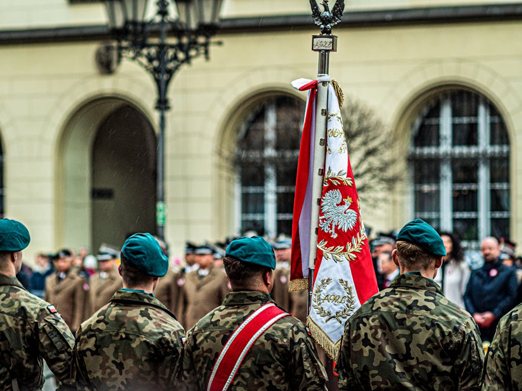 Polish soldiers in uniform during a ceremonial parade with national flag.